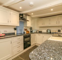 A kitchen with white cabinets black countertop sink microwave oven and various kitchen appliances at Cousham Cottage in Kingsand And Cawsand