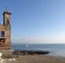 A clock tower next to a rocky beach and ocean with a boat on the water at Nirvana Kingsand And Cawsand