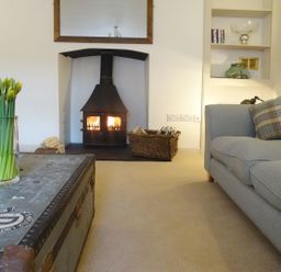 A living room with a fireplace a basket of firewood a blue sofa and a vase of daffodils on a metal trunk table at Nirvana Kingsand And Cawsand