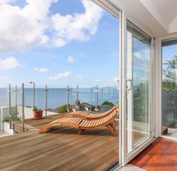 A wooden deck with two lounge chairs and glass railing overlooking the ocean at Rock Rose in Downderry
