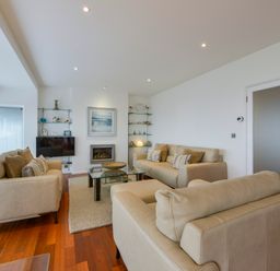 A living room with beige sofas a glass coffee table and shelves with decorations at Rock Rose in Downderry