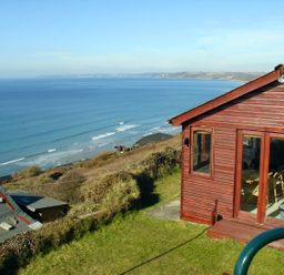 A wooden cabin on a grassy hill overlooking the ocean with waves near Seagulls Nest in Whitsand Bay near Millbrook