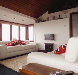 A sitting area with white sofas and Union Jack pillows near windows at Seagulls Nest Whitsand Bay near Millbrook