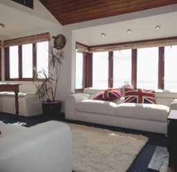 A living room with white sofas and Union Jack cushions and a wooden dining table at Seagulls Nest in Whitsand Bay near Millbrook