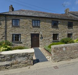 A stone cottage with six windows and a dark wooden door with plants along the front at Samuels Cottage in Lanreath