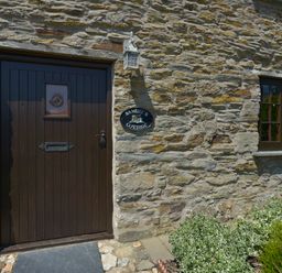 A stone wall with a dark wooden door and window with plants below at Samuels Cottage in Lanreath