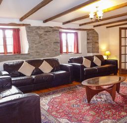 A sitting room with three black leather sofas a red patterned rug a wooden coffee table and exposed stone walls at Samuels Cottage in Lanreath