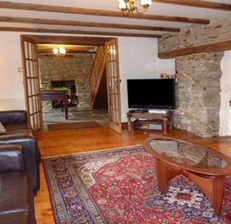 A living room with a leather sofa a glass coffee table a television and an adjoining room with a pool table at Samuels Cottage in Lanreath