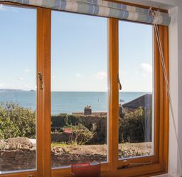 A window with a view of the sea trees and rooftops at Chough Cottage in Kingsand And Cawsand