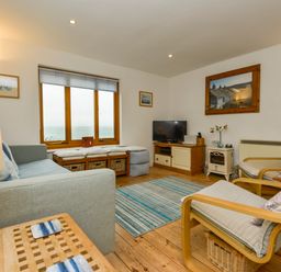 A living room with a sofa chairs a television and a window with a sea view at Chough Cottage in Kingsand And Cawsand