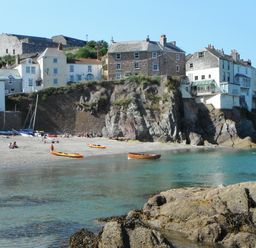 A rocky beach with kayaks and people near coastal houses on cliffs at Balcony Cottage in Kingsand And Cawsand
