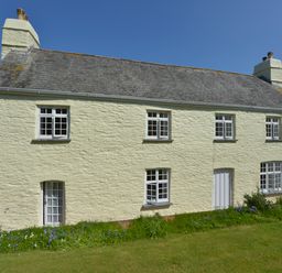 A two-story stone house with multiple windows and a door in a grassy garden at Tregonhawke Farmhouse in Millbrook