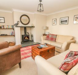 A living room with two beige sofas a brown armchair a wooden chest coffee table a fireplace and wall shelves with books at 1 River Cottage Calstock