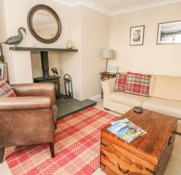 A living room with a beige sofa and brown armchair near a fireplace with a round mirror and a wooden chest coffee table at 1 River Cottage in Calstock