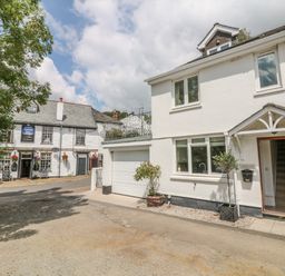 An exterior view of a white house with open door and garage next to a white building with hanging flower baskets and sign at 1 River Cottage in Calstock