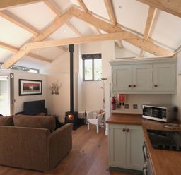 An open plan living room and kitchen with wooden ceiling beams a stove a sofa and kitchen cabinets at Mugwell Barn Luckett near Callington