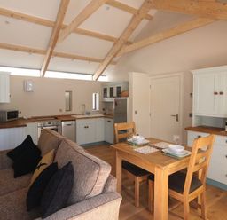 A kitchen and dining area with wooden beams on the ceiling a wooden dining table and chairs a sofa and white cabinets at Mugwell Barn Luckett near Callington
