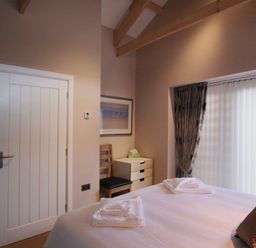 A bedroom with a bed towels a wooden chair a small chest of drawers and a window with curtains at Mugwell Barn Luckett near Callington