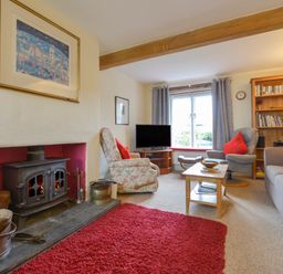 A living room with a wood-burning stove red rug armchairs sofa coffee table and bookshelf at Regatta Cottage in Feock