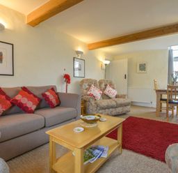 A living room with sofa and armchairs a coffee table with magazines a dining table near a window at Regatta Cottage in Feock