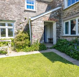 An outdoor area with stone walls a wooden bench green plants and a grassy lawn at Polcreek Farmhouse in Veryan