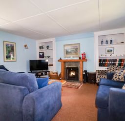 A living room with blue sofas a fireplace and a television at Polcreek Farmhouse in Veryan
