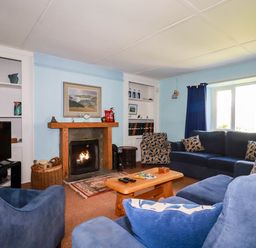 A living room with blue sofas a wooden coffee table a fireplace and built in shelves at Polcreek Farmhouse in Veryan