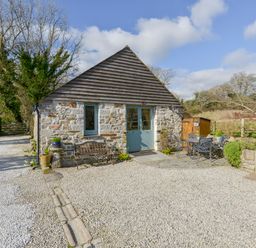 A small stone and wood cottage with a bench and an outdoor table with chairs at Hideaway Barn in Charlestown