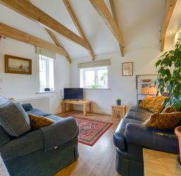 A living room with exposed wooden beams two sofas a small TV on a wooden table and a potted plant at Hideaway Barn in Charlestown