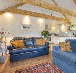 A living room with two blue sofas with patterned cushions a wooden floor and exposed wooden beams at Hideaway Barn in Charlestown