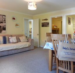 A living room with a sofa and cushions next to a dining table with chairs and flowers at Stones Throw in St Mawes