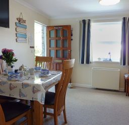 A dining area with a wooden table set for four next to a window and an open door at Stones Throw in St Mawes