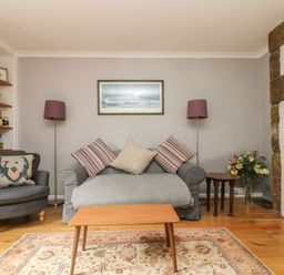 A living room with a sofa and armchair with cushions a coffee table and a fireplace at Primrose Cottage in Penryn