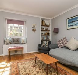 A living room with a grey sofa and armchair a wooden coffee table and a window seat with cushions at Primrose Cottage in Penryn