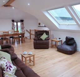 A living room with brown leather furniture wooden dining table and large skylight windows at The Hayloft in Breage