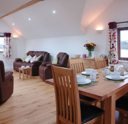 A dining table set with white dishes and cups next to a seating area with brown leather sofas and floral curtains at The Hayloft in Breage