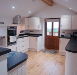 A kitchen with white cabinets black countertops wooden floor and a wooden door at The Hayloft in Breage