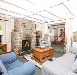 A living room with stone fireplace coffee table and chairs at Badger Cottage in Mawgan-in-Meneage near Helston