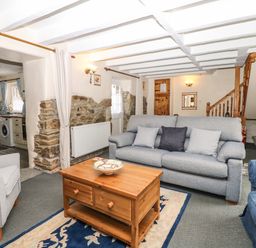A living room with sofas a wooden coffee table and a doorway to a kitchen at Badger Cottage in Mawgan-in-Meneage near Helston