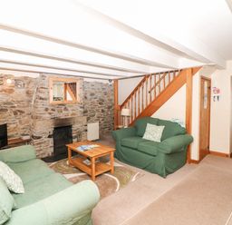A living room with stone walls green sofas a wooden coffee table and a staircase at Swift Cottage in Mawgan-in-Meneage near Helston