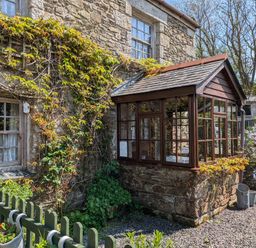 A stone cottage with a wooden framed glass porch and climbing plants at Swift Cottage in Mawgan-in-Meneage near Helston
