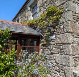 Exterior stone wall of a cottage with wooden framed windows and flowering plants at Swift Cottage in Mawgan-in-Meneage near Helston