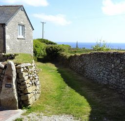 A stone house with a pathway and stone walls leading to the sea at The Studio in Rinsey Cove near Praa Sands