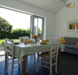 A dining area with a table set for four and a gray sofa with yellow cushions at The Studio in Rinsey Cove near Praa Sands