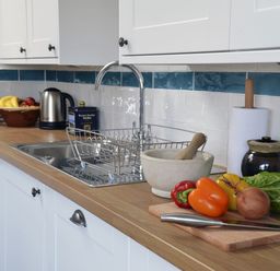 A kitchen counter with vegetables on a cutting board a knife a mortar and pestle a glass of wine and a sink at The Studio Rinsey Cove near Praa Sands