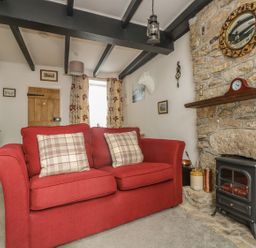 A living room with a red sofa and plaid cushions a stone fireplace with a clock and a mirror at Mollys Cottage in St Just