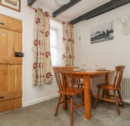 A dining area with a wooden table and three chairs near a window with floral curtains at Mollys Cottage in St Just