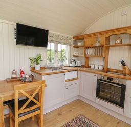 A kitchen with wooden cabinets a table and chairs a wall mounted television and a window at Hillside View in Rhayader
