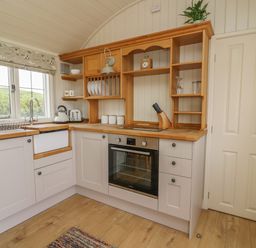 A kitchen with white cabinets wooden countertops an oven a window and shelves at Hillside View in Rhayader