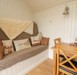 A corner with a cushioned bench with animal print pillows and a wooden dining table with chairs at Hillside View Rhayader